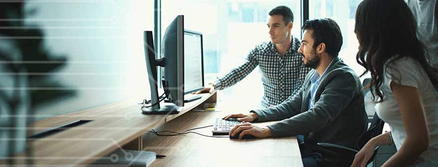 Two men and a woman studying a computer screen as part of their cyber security analyst roles.