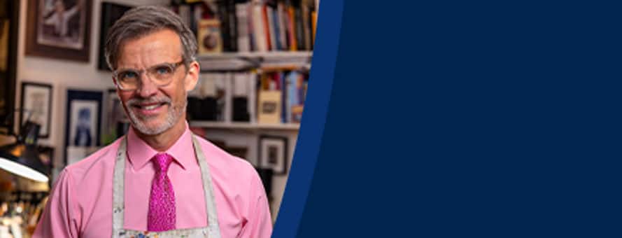 Dale Stephanos, a 2023 graduate from SNHU, standing in his studio and wearing an apron covered in paint.