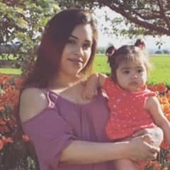 Dayana Sanchez, a military spouse scholarship recipient, holding her daughter in front of flowers.