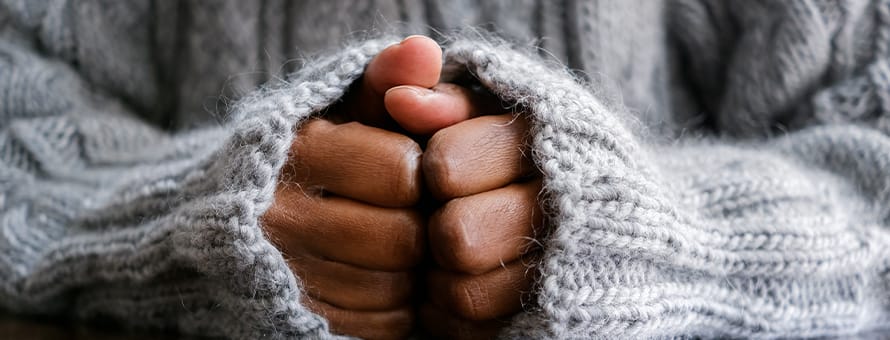 Someone's hands curled in a gray knit sweater as they manage their anxiety