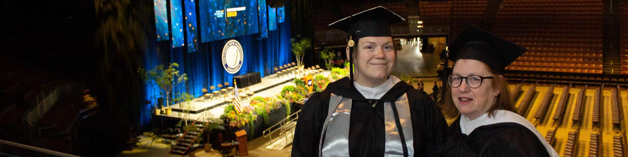 Delaware residents and SNHU graduates Jenny Gardner and Susan Lasala wearing their cap and gowns in the SNHU Arena for Commencement.