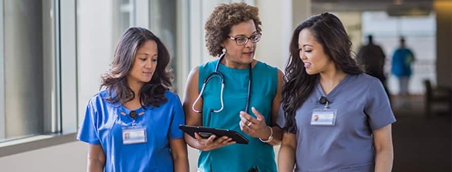 Three nurses at different career levels walking in a hospital corridor.
