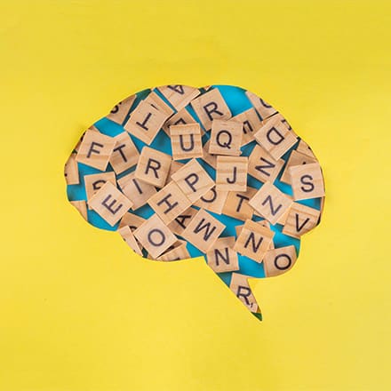 A speech bubble cut from a yellow background and filled with wooden blocks with letters on them.
