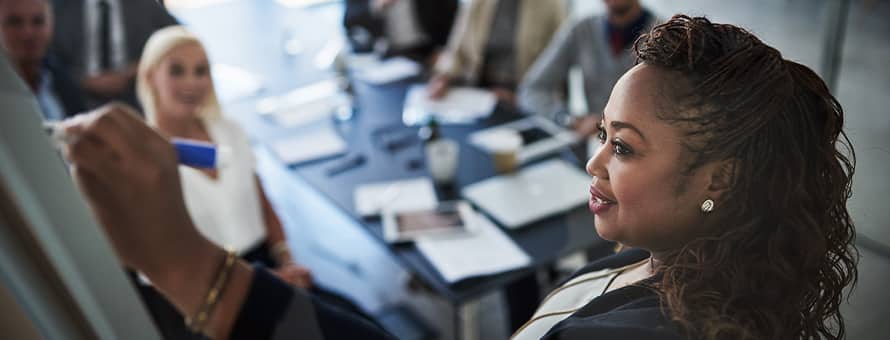 A woman writes on a whiteboard while talking to a small group of people