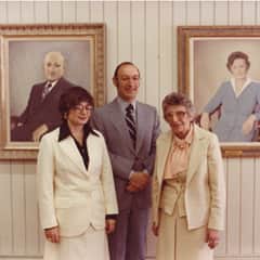 Three people standing in front of two painted portraits.
