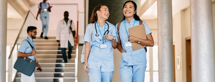 Two nurses dressed in scrubs and carrying backpacks for the class they're getting continuing education credits from.