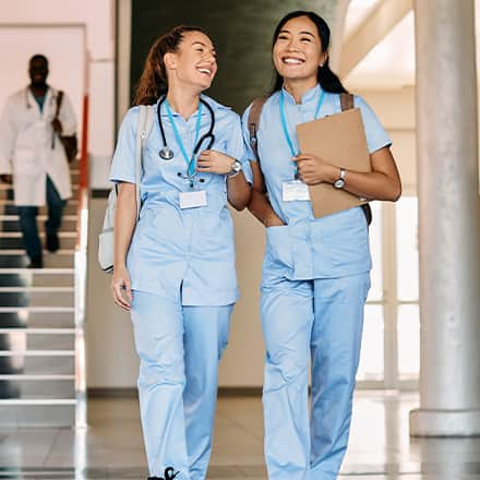 Two nurses dressed in scrubs and carrying backpacks for the class they're getting continuing education credits from.
