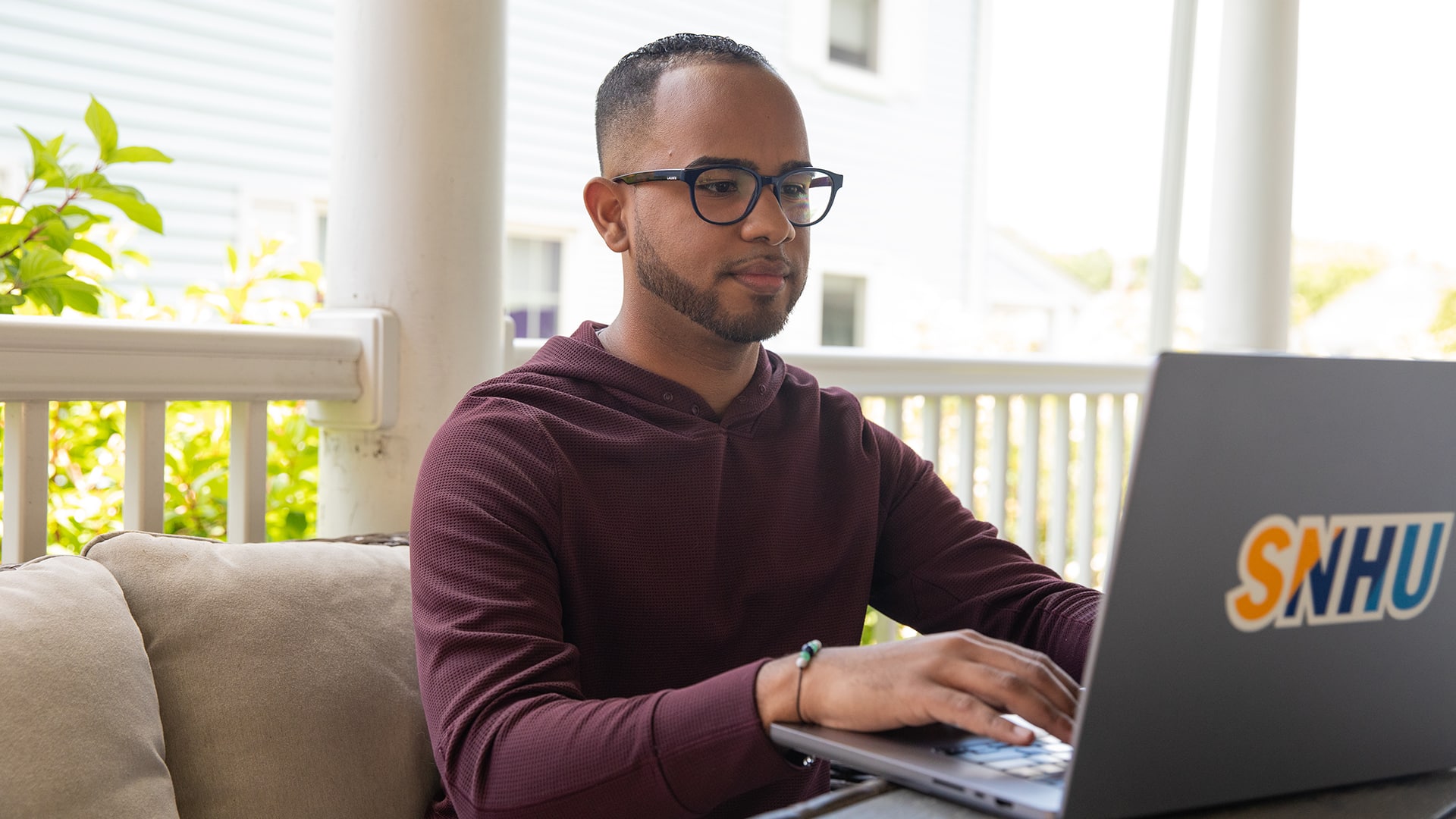 Geremy Laboy, who earned his degree at SNHU, sitting on his porch and typing on his laptop.