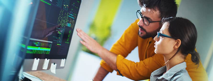 A student getting experiential learning in programming with the support of a professional who is pointing at the computer.