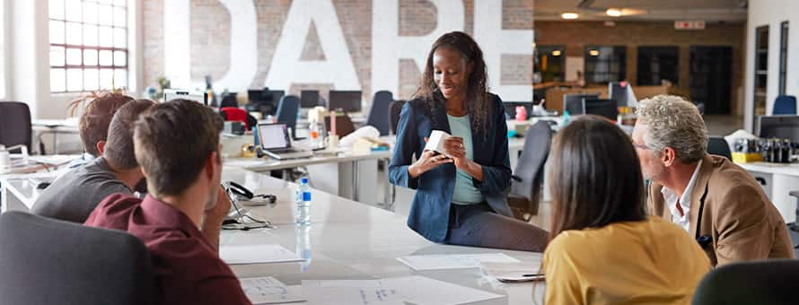 Six marketing professionals sitting around a white office table, discussing a product.