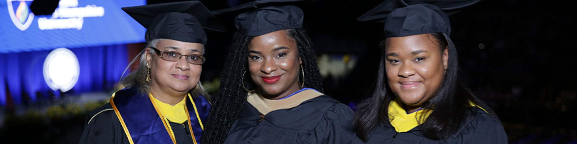 SNHU graduate and Georgia resident Kellann Alves standing between her mother Sabrina Mentis and sister Stephanie Mentis, all wearing their cap and gowns.