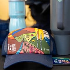 The official SNHU Global Days of Service hat for 2025, blue with a colorful illustration of diverse landscapes such as a garden, mountains, dessert and ocean.