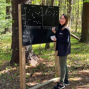 A Global Days of Service volunteer in the SNHU Arboretum, writing on a chalkboard.