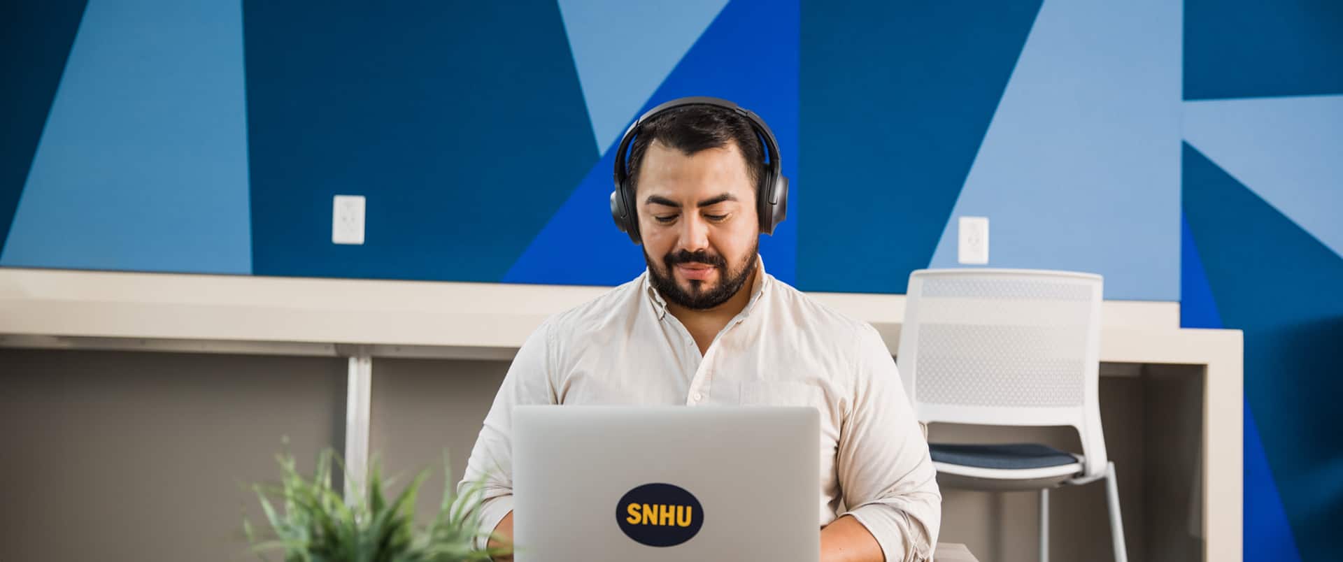 Jesus Suarez, who earned his bachelor's degree in graphic design and media arts in 2021, wearing headphones and typing on a laptop that has an SNHU sticker on the cover.
