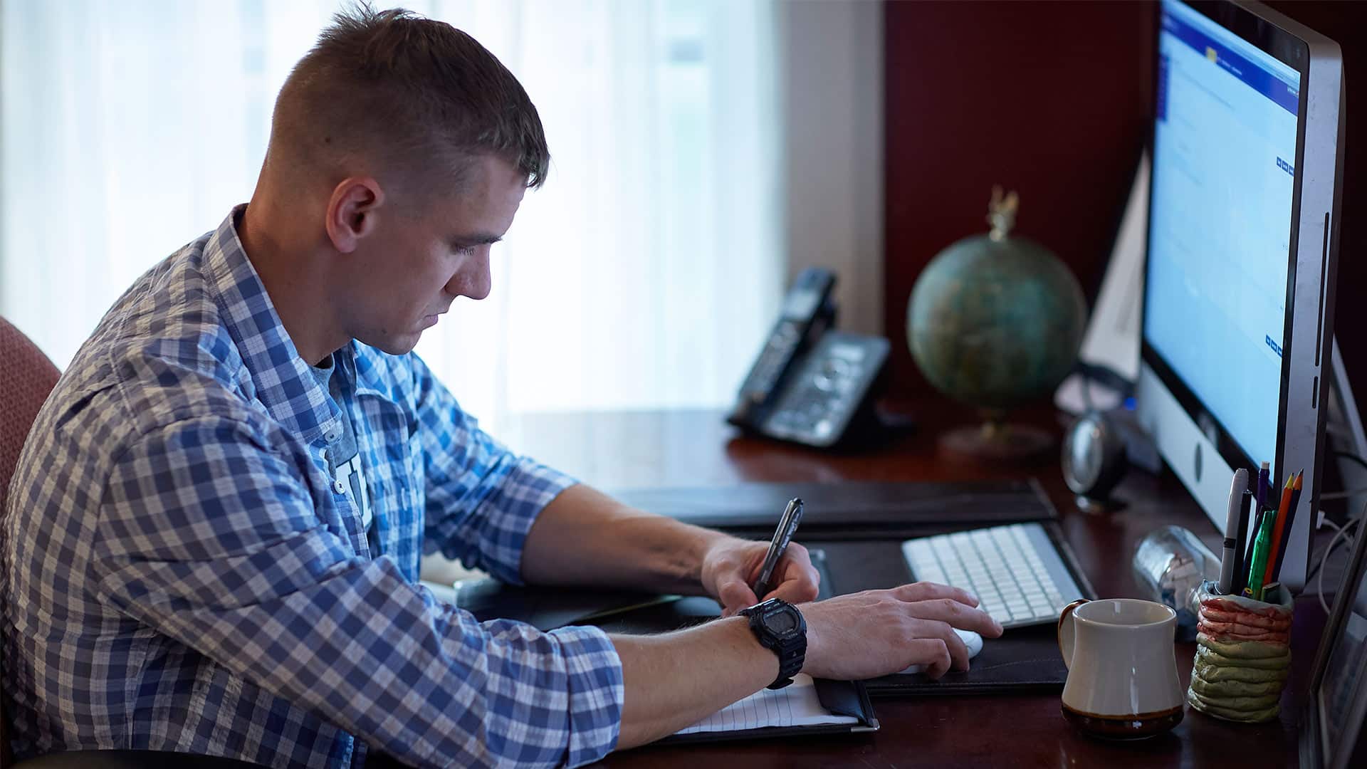 Michael Leathers, who earned a degree from SNHU in 2016, sitting at a desk with a computer monitor in front of him  and writing in a notebook with his left hand.