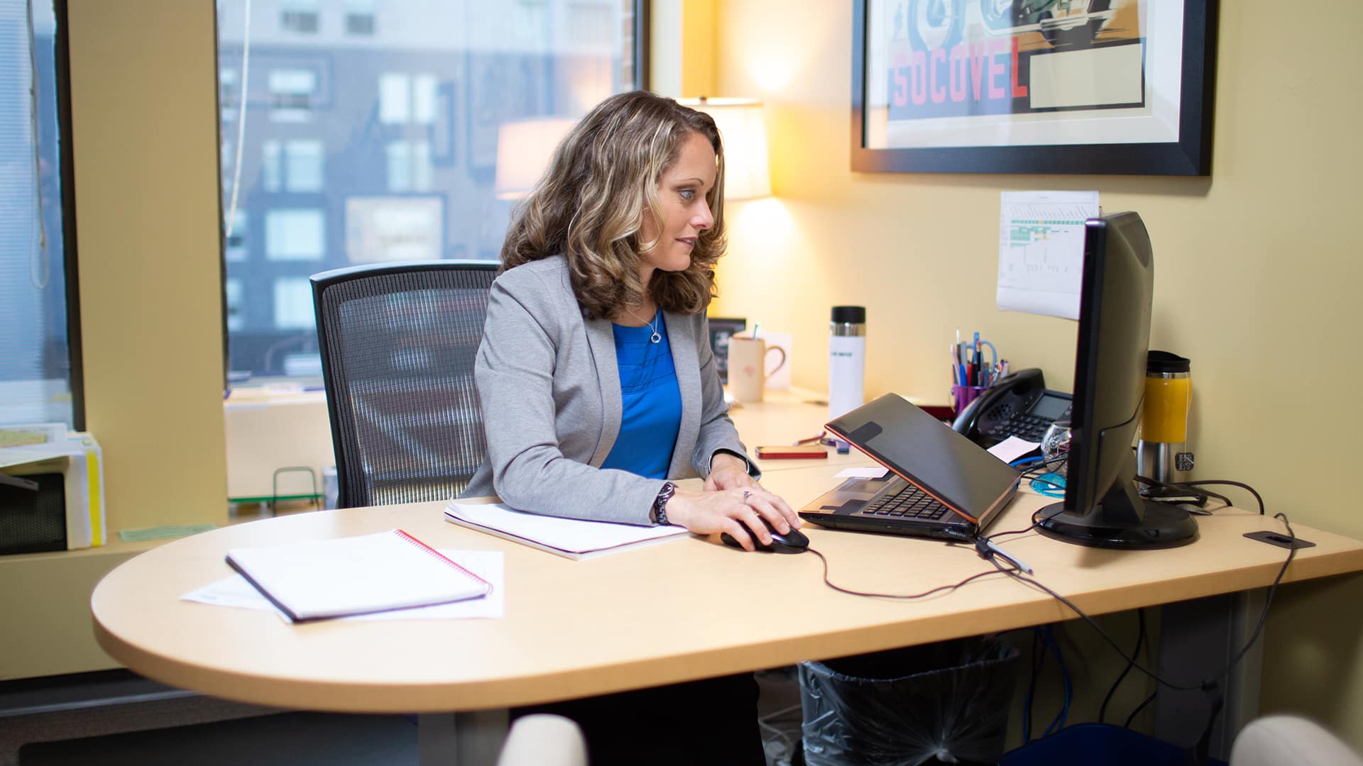 Kerry Smith, who earned her degree from SNHU, sitting at an office desk, using a mouse and looking at a  computer monitor.