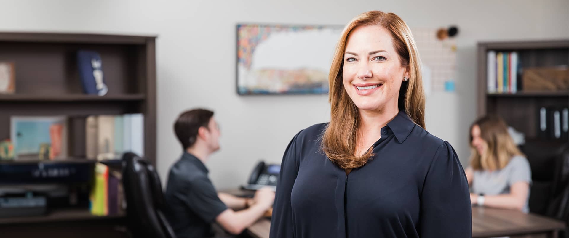 Nikki Bennett, who earned her MBA from SNHU, standing in an office with two people seated at a table and bookshelves in the background.