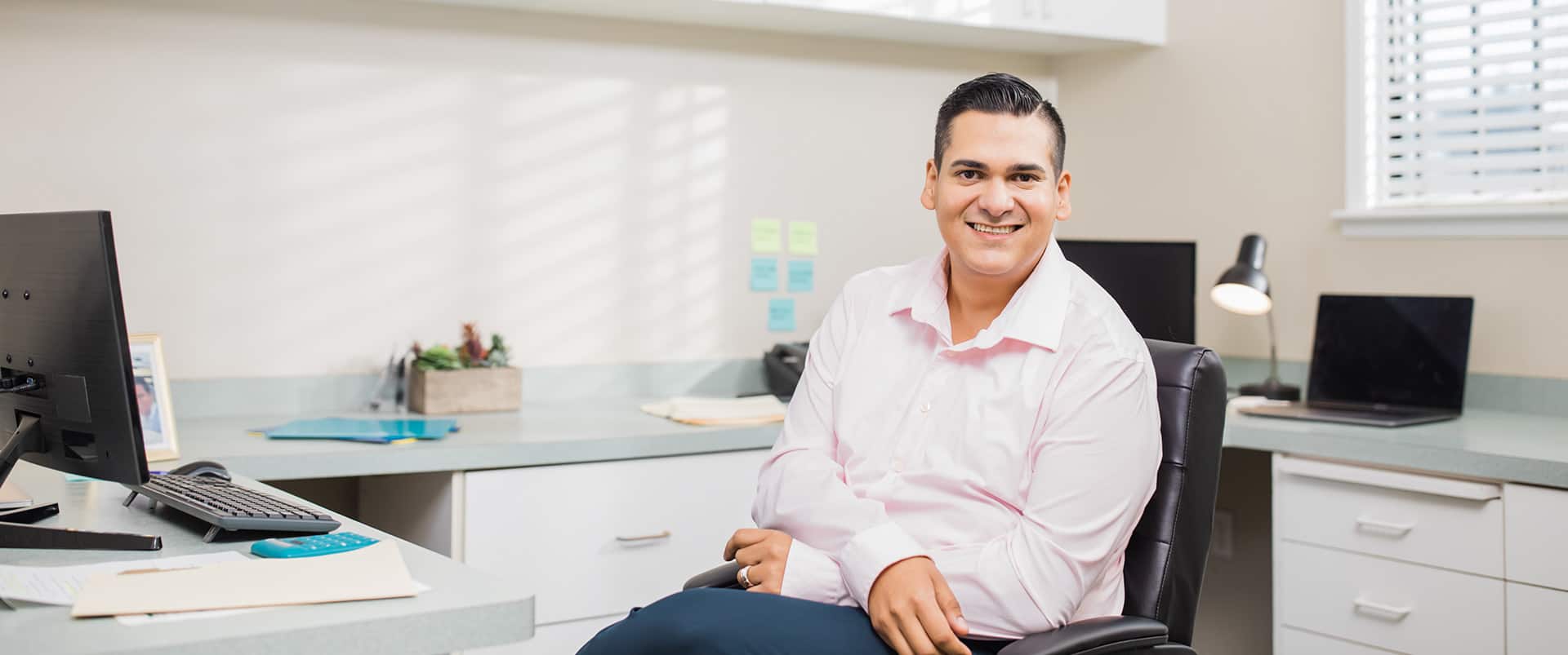 Juan Muños, who earned his degree from SNHU in 2022, sitting in an office chair with one leg crossed  over the other.