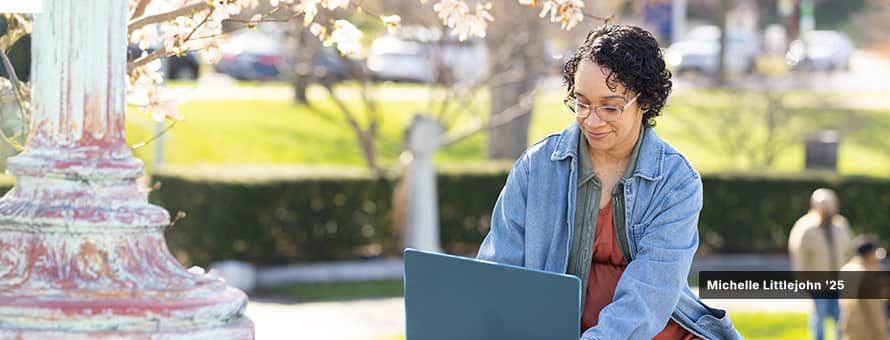 Michelle Littlejohn '25, who earned her BA in Graphic Design & Media Arts from SNHU, studies from a park bench on her laptop computer.