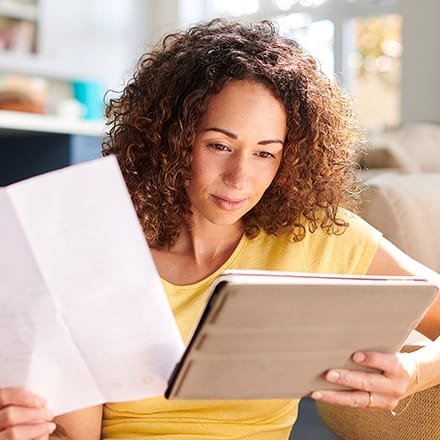 An online student learning how financial aid works as she holds her financial aid offer letter and reviews information on a tablet.