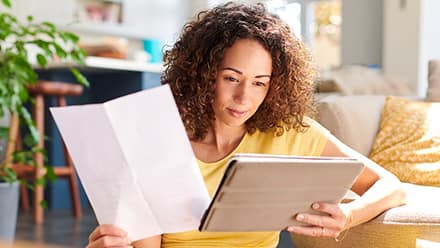 An online student learning how financial aid works as she holds her financial aid offer letter and reviews information on a tablet.
