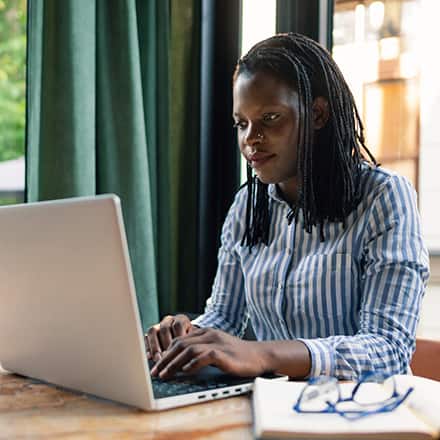A woman sitting at a table on her laptop working towards her associate degree