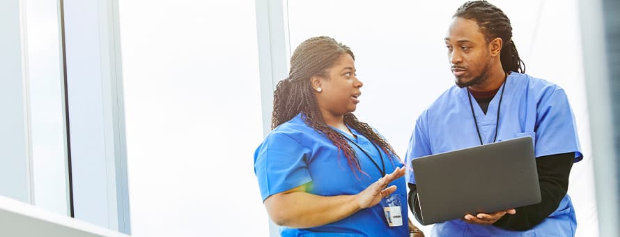 Two nurses working on a laptop while discussing how long it takes to become a nurse