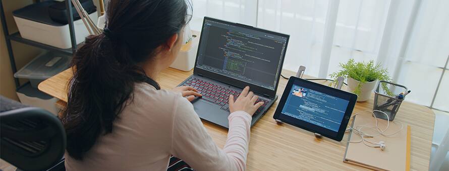 A computer science master's student programming on a laptop with a tablet next to it.