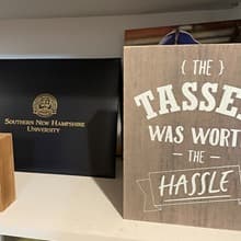 A diploma coverwith the text Southern New Hampshire University and a sign with the text The tassel was worth the hassle