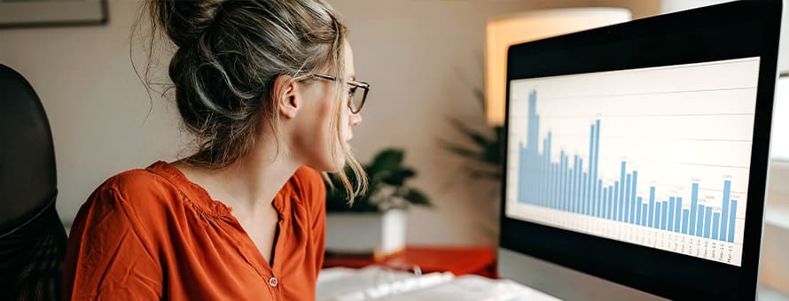 A professional who learned how to become a data analyst, sitting in front of a computer with a bar graph on the screen.