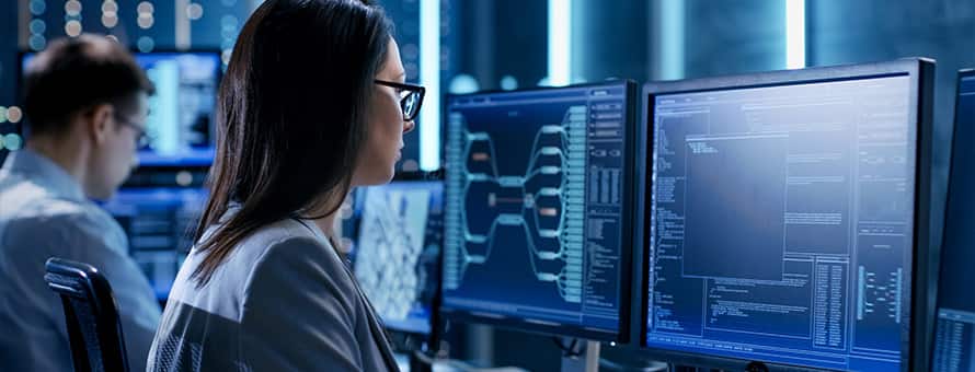 A woman sitting in front of two computer monitors after she learned how to become a cyber security professional.