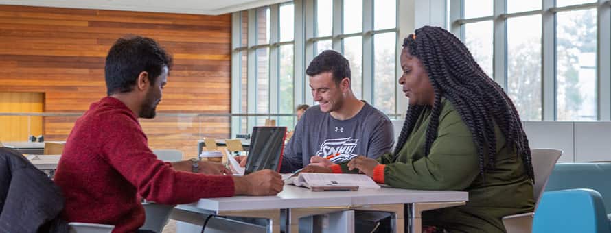 Three first-year college students sitting around a table and doing homework.