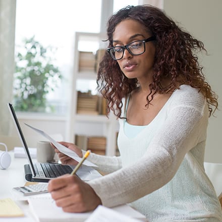 A person at a table, reviewing documents and taking notes in a notebook on how to get a master's degree.