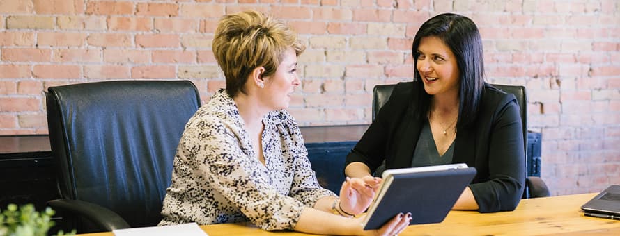 Two professionals in HR roles at an office table, reviewing information on a tablet.