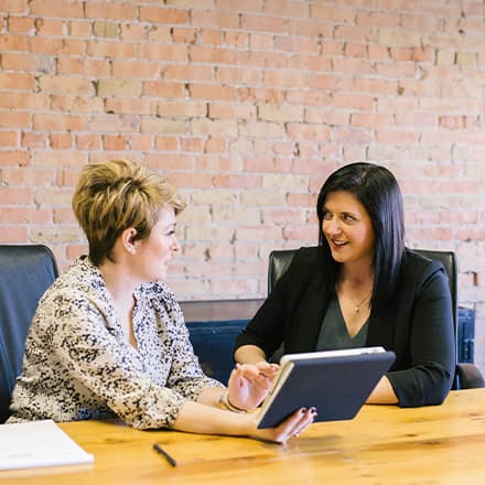 Two professionals in HR roles at an office table, reviewing information on a tablet.