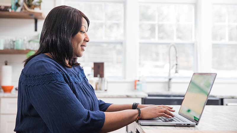Monique Gray, who earned her degree from SNHU in 2022, typing on her laptop on her kitchen counter.