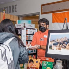An SNHU student standing behind a booth at the culture fair, handing good to an attendee.