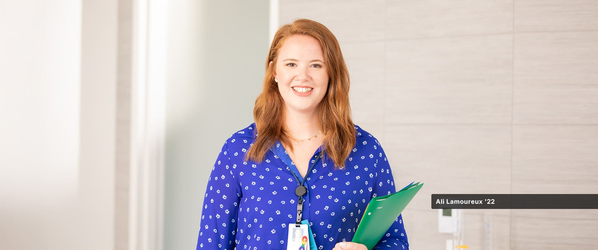 Ali Lamoureux-Rule, who earned her healthcare administration degree from SNHU in 2022, wearing a blue and white blouse and holding a green folder in her left arm.
