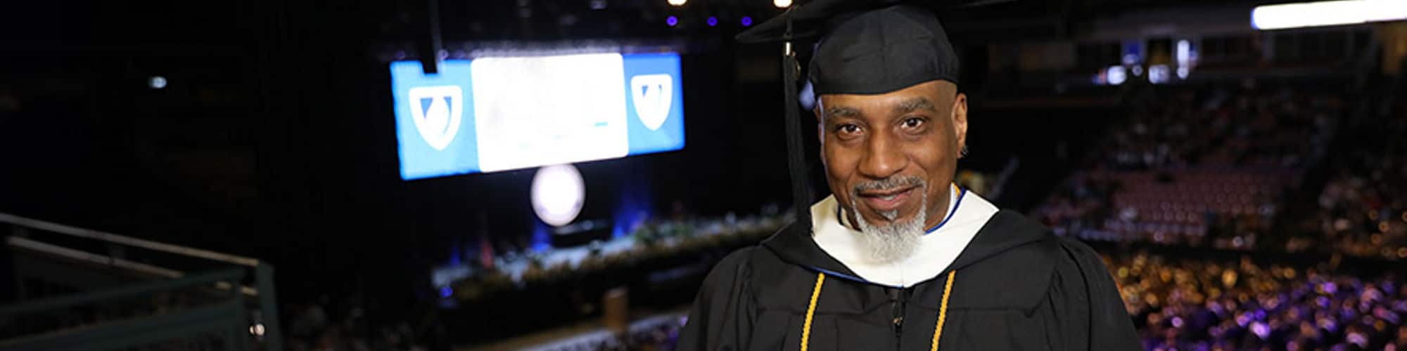 Billy Moore, who earned a bachelor's in general studies in 2023, wearing his cap and gown and holding his diploma inside the SNHU Arena at a Commencement ceremony.