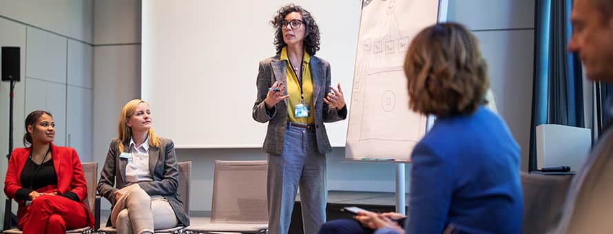 An industrial-organizational psychologists standing at the front of the room presenting to other psychologists. 