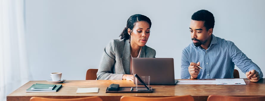 Two people wearing professional clothes looking at a laptop to see if an online associate in finance is worth it