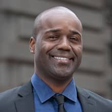 Jean Besson, who earned his bachelor's in business administration in 2014, wearing a blue button down shirt and dark sports coat.