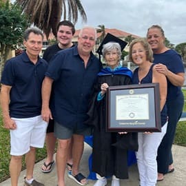 Joan Donovan dressed in graduation cap and gown, holding her SNHU diploma while surrounded by 5 family members.