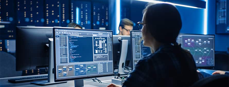 A woman with a ponytail and glasses coding in a computer lab.