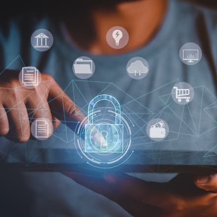 A person using a tablet with icons hovering in the air, including a blue lock to represent cybersecurity.