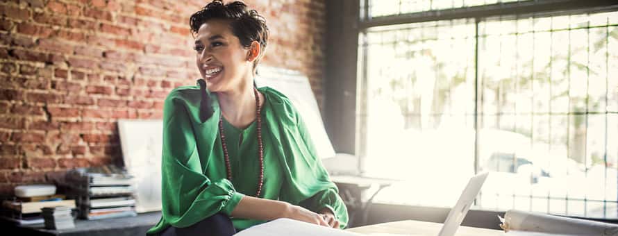A woman in a green shirt sitting at a desk with a laptop, working in a bachelor's degree job