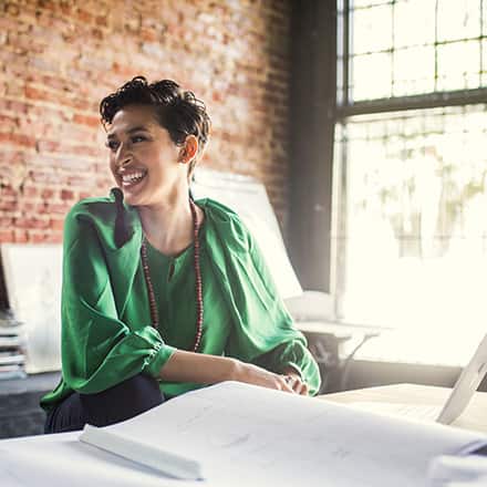 A woman in a green shirt sitting at a desk with a laptop, working in a bachelor's degree job