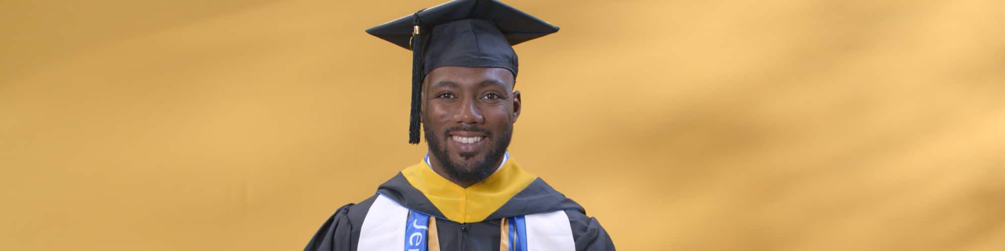 Jerron Trice, a Kentucky resident and SNHU graduate, wearing his cap and gown and holding a blue pennant with Kentucky in gold lettering.