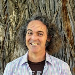 Larry Burns, an adjunct humanities instructor at SNHU, wearing a button down shirt and standing in front of a tree.