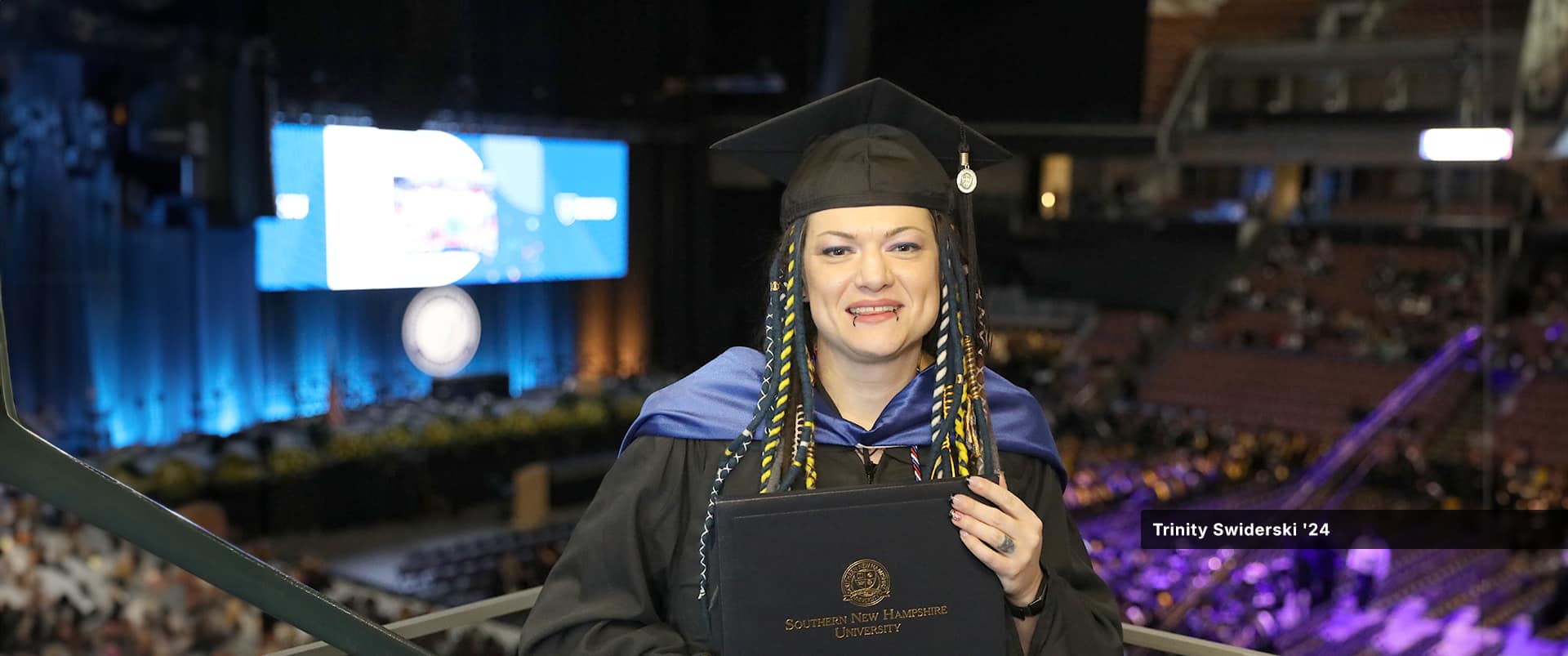 Trinity Swiderski, who earned her master's in communication from SNHU in 2024, wearing her cap and gown and holding her diploma at the SNHU commencement ceremony.
